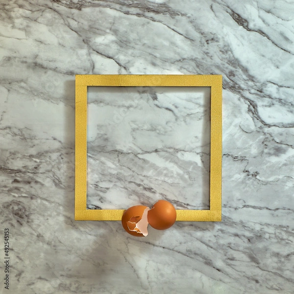 Fototapeta Egg shells on a gold frame. Gray marble background. Text space. Top view. Minimal style. Food, Easter.
