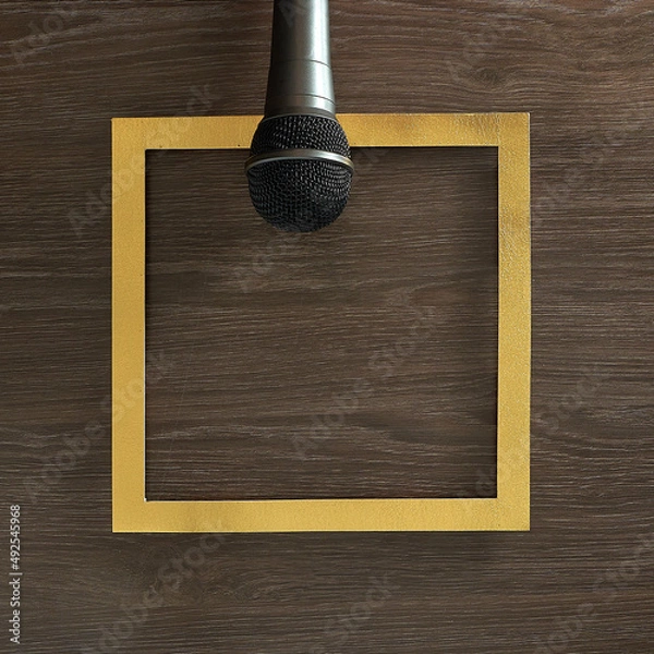 Fototapeta Microphone on a gold frame on a wooden background. Text space. Top view. Minimal style.