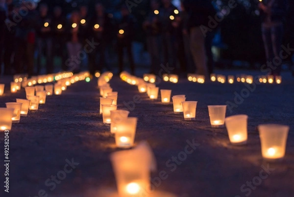 Fototapeta A group of candles burning in street and people in the background.