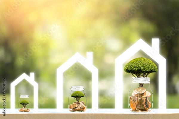 Obraz Bottle bank and gold coin and the tree growing on the top put in the home with shape transparent screen on sunlight in the public park, Saving or investment for buy a real estate and house concept.