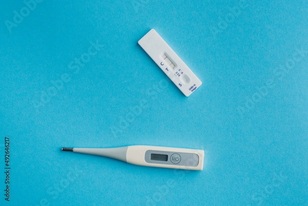Fototapeta Express test for covid-19 with a positive result and a thermometer on a blue solid background.