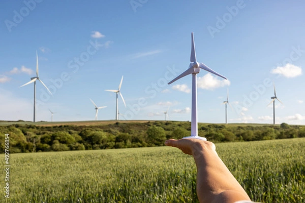Fototapeta Engineer in the fields holding a wind turbine model with real ones on background