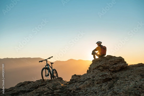 Obraz Cyclist mtb biker sits and relax on mountain top at sunset