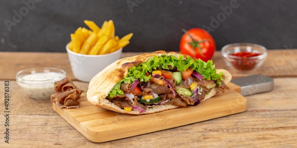 Obraz Döner Kebab Doner Kebap slice fast food in flatbread with French Fries on a wooden board panorama