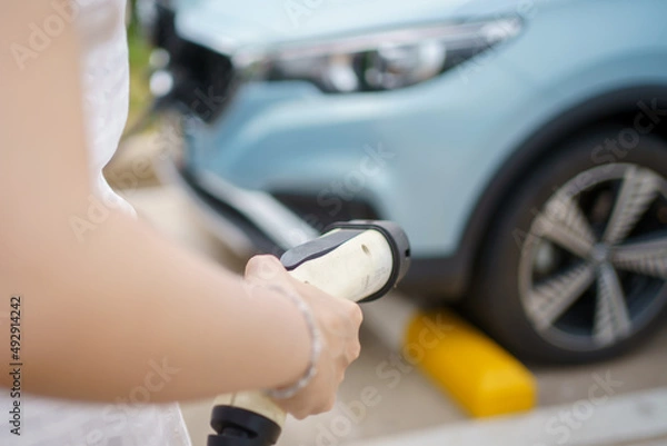 Obraz Unrecognizable Asian woman holding a DC - CCS type 2 EV charging connector at EV charging station.