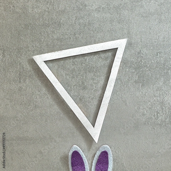 Fototapeta Bunny white purple ears and a triangular text frame on a gray concrete background. Text space. Top view. Minimal style.
