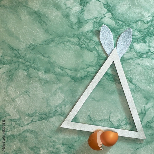 Fototapeta Silver triangle. Rabbit white ears and egg shells on a green marble background. Text space. Top view. Minimal style.