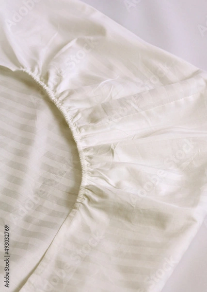 Obraz Corner of the sheet with sewn-in elastic band for a good fit on the mattress and a comfortable sleep. White fabric for mockup overlay design. Home textiles for the bedroom. Linen in stripe satin 