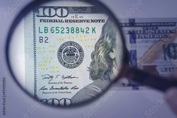 Fototapeta Magnifying glass on the background of a 100 dollars close-up. Concept on the theme of checking money for authenticity.