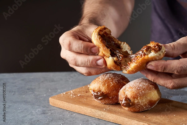 Fototapeta man's hand breaking a Berliner stuffed with dulce de leche