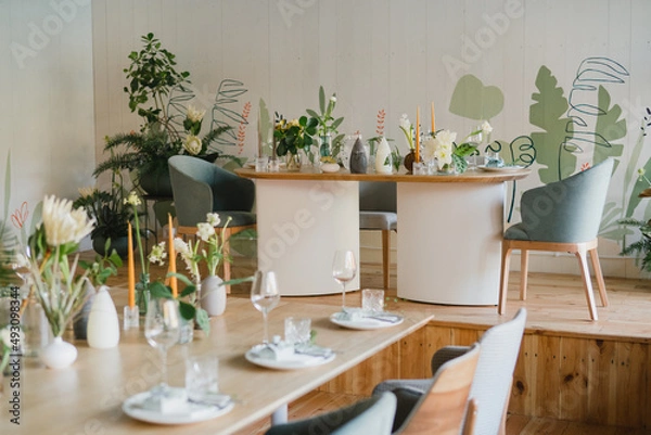 Fototapeta Coziness and style. Modern event design. Table setting at wedding reception. Floral compositions with beautiful flowers and greenery, candles, laying and plates on decorated table.