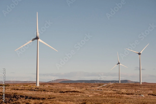 Fototapeta High wind power turbine in a field. Cloudy sky background. Renewable green energy production, source of clean electric supply. Modern technology and design. Nobody.