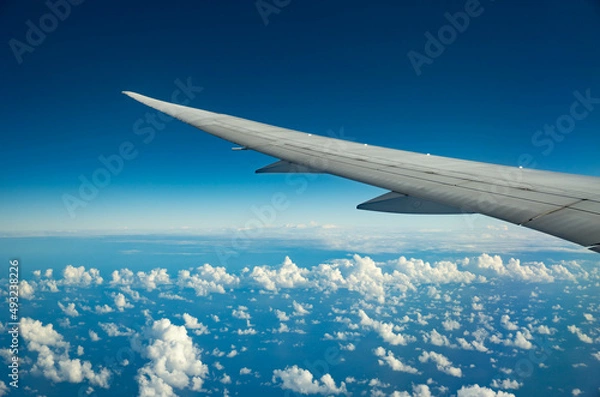 Obraz Wing of an airplane flying over morning clouds. View on cloud and blue sky through the airplane window.