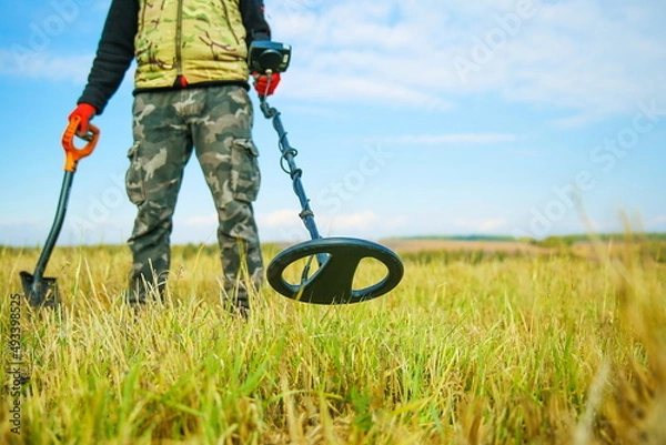 Fototapeta man holds a metal detector in nature in search of treasure. close-up demining