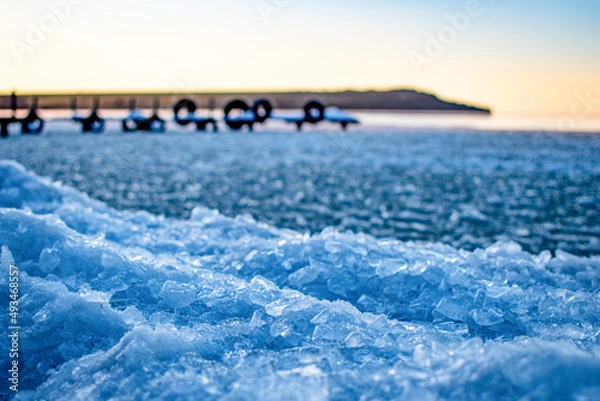 Fototapeta Pieces of ice on the background of the bridge and the hill, near the water
