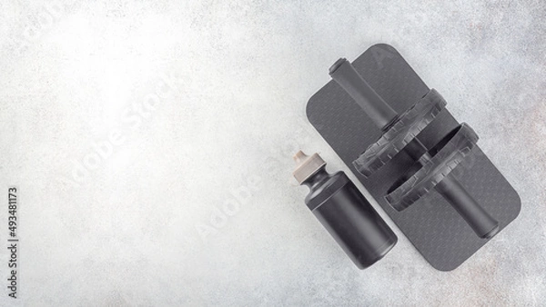 Obraz Black ab roller with mat, sport bottle of water on a gray concrete background, top view, copy space. Home workout. Fitness and activity. 