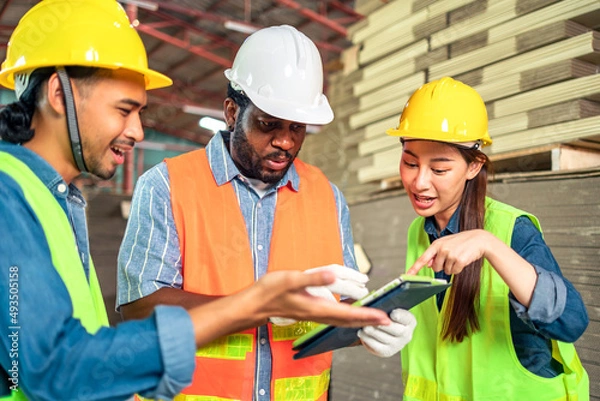 Fototapeta Engineer african man and asian worker wearing safety helmet and vest holding notebook and take note on the paper  warehouse.Products and corrugated cardboard. Factory for the manufacture.