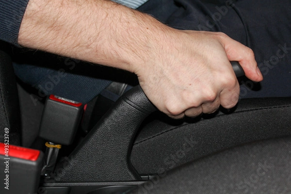 Fototapeta Close-up of a man's hand in a rubber glove pulling the handbrake lever in a car. The driver pulls on the handbrake in the car to activate the parking brake, the importance of the parking brake.
