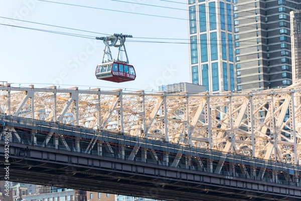 Fototapeta Roosevelt Island Tramway runs beside the Queensboro Bridge toward the high-rise residential building in Midtown Manhattan from Roosevelt Island on November 2021 New York City NY USA.
