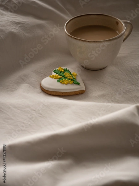 Fototapeta Morning coffee with milk with heart-shaped cookies painted with mimosa pattern icing  on a white bed in the morning light