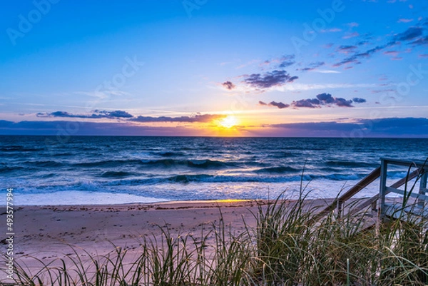Fototapeta Sunrise on the beach in the Atlantic Ocean, Melbourne Beach, Florida. View from the veranda of a private house in the early morning. The sun shines through the clouds and is reflected in the restless 