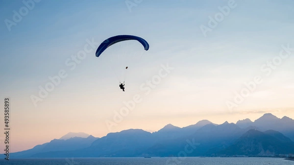 Fototapeta Silhouette of a man on a paraglider flying over the sea at sunset.