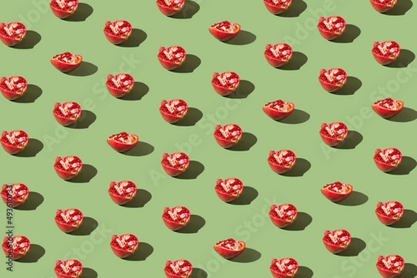 Fototapeta Creative pattern made of half fresh pomegranates on green background with shadows. Refreshment concept. Healthy food ingredient theme.