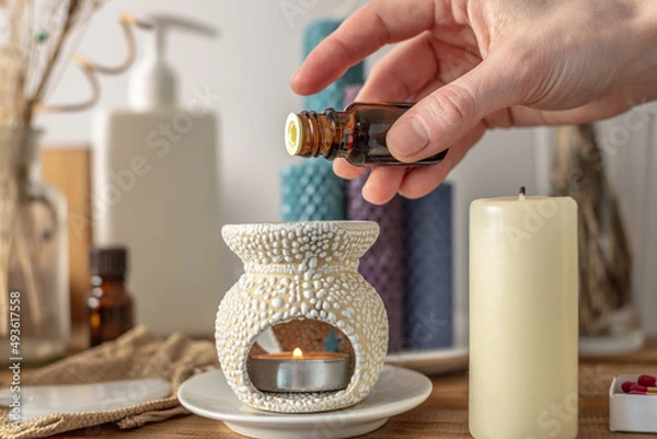 Obraz Female hand is holding a bottle of essential oil and dripping it in an aroma lamp for aromatherapy and calm relaxing atmosphere, concentration on meditation, care procedures and other rituals