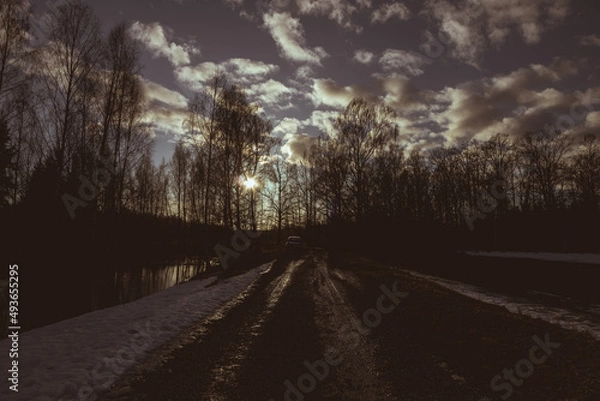Fototapeta dark muddy wet dirt road in countryside, evening sunset, snow, mud, sunlight