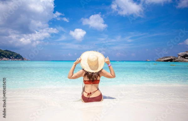 Fototapeta back view of woman wearing a straw hat and orange bikini relax on the beach with beautiful blue sky.at Similan island Phuket Thailand , summer vacation concept