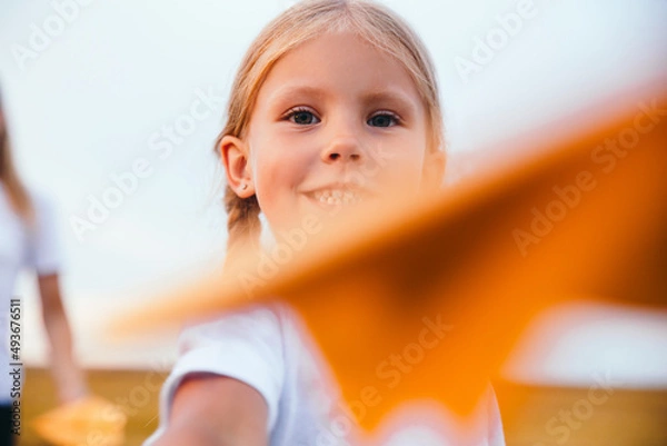Obraz Cute child girl running and playing toy paper airplane in the field in summer day