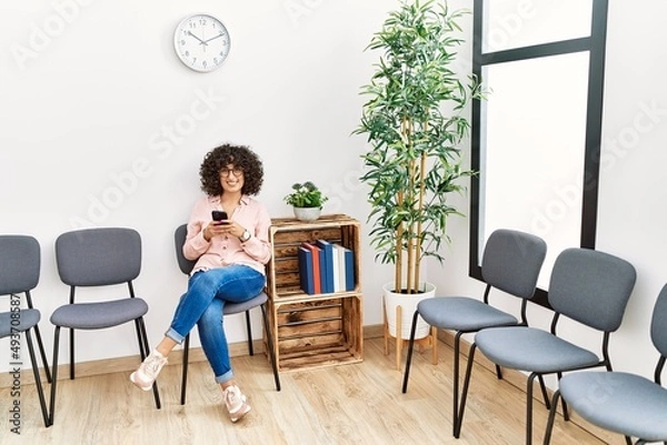 Fototapeta Young middle east woman using smartphone sitting on chair at waiting room