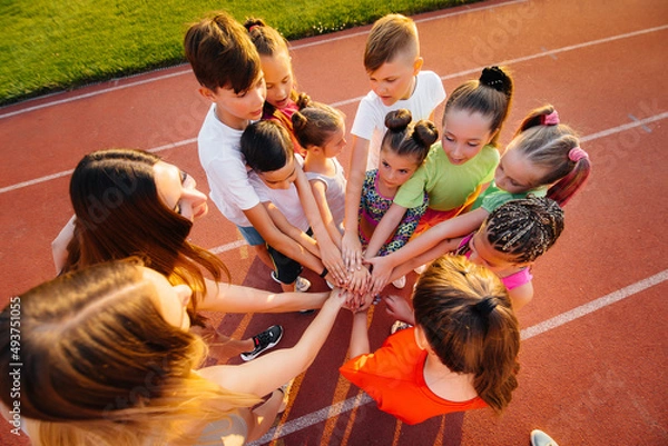 Fototapeta A large group of children, boys and girls, stand together in a circle and fold their hands, tuning up and raising team spirit before the game at the stadium during sunset. A healthy lifestyle.