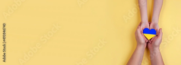 Obraz A narrow photo of a man's hands holding the hands of a child with a heart with the flag of Ukraine.