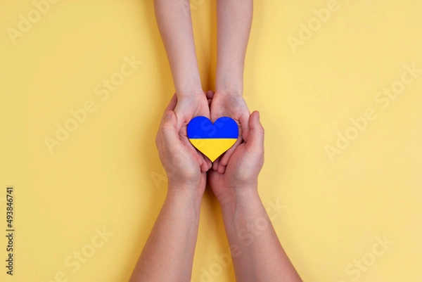 Fototapeta Men's hands hold the hands of a child and a heart with the flag of Ukraine. People don't want a war in Ukraine.