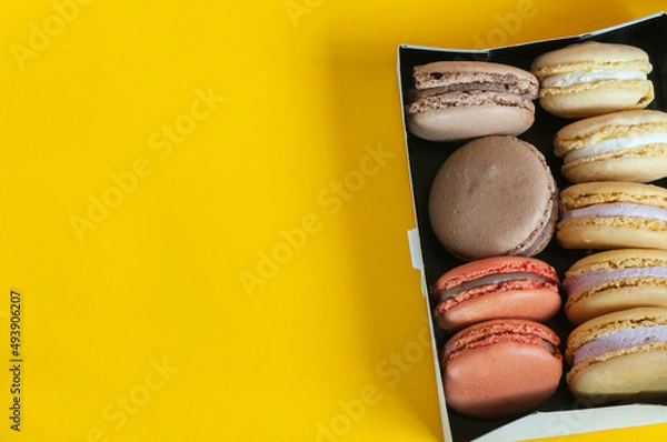 Fototapeta Multi-colored macaroons in a box on a yellow background. Top view, natural light. Selective focus with copy space