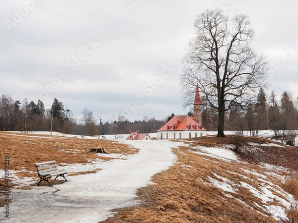 Fototapeta Early spring in the city park, the remains of snow on the alley to the castle. Spring view of the ancient Maltese Palace in Gatchina Park, Russia.