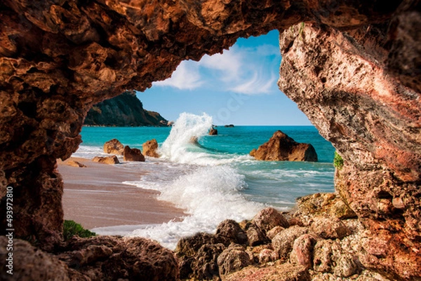 Fototapeta Beautiful magical view of the beach with heavy waves through a hole in the rock