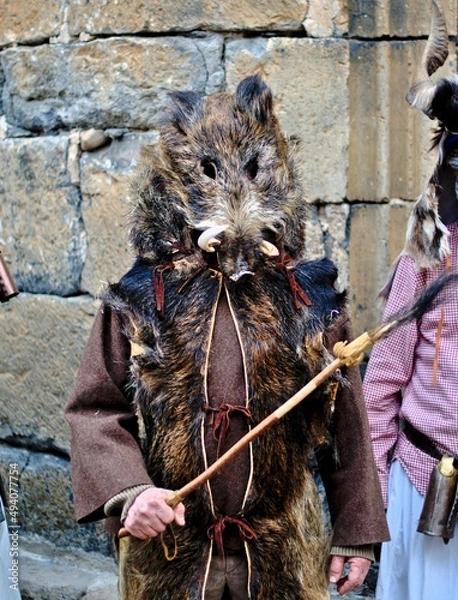 Fototapeta Enciso, Spain – March 5, 2022: Man disguised with skins and boar's head. Wooden stick with a boar's tail at the end. Traditional carnival of Enciso.