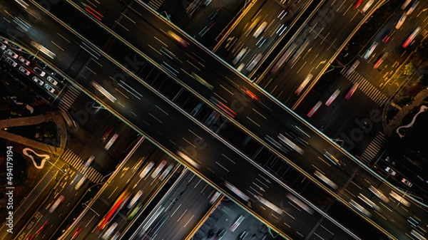 Fototapeta Aerial top down of multilevel elevated road huge traffic junction in modern metropolis city. Night long exposure motion blur of vehicles. Modern development of infrastructure and motorways in China.