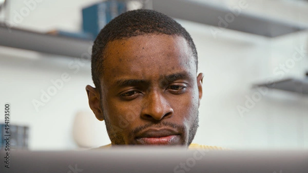 Fototapeta Young african freelancer man working on computer at home. Serious man work at home