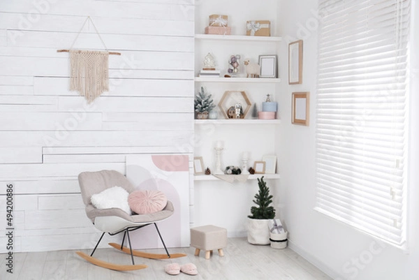 Fototapeta Stylish room interior with rocking chair, wall shelves and beautiful Christmas decor