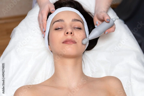 Fototapeta A girl's face in close-up during a facial treatment at a cosmetologist.The cosmetologist does biomechanical stimulation of the face to the client.The concept of professional cosmetology.