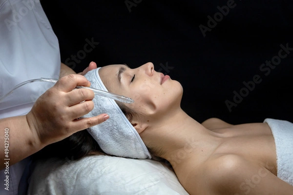 Fototapeta A cosmetologist does a gas-liquid peeling procedure for a young girl.A girl in the cosmetologist's office during the procedure.Face and neck care in a beauty salon.Cosmetic procedures for the face