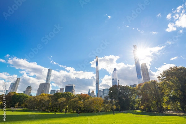 Fototapeta The sun shines among clouds over the Ultra-luxury high-rise residential skyscraper in Billionaires's Row beyond the Sheep Meadow at Central Park in autumn on November 03, 2021 at New York City NY USA.
