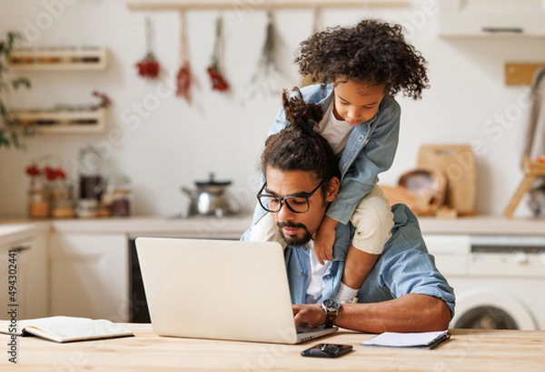 Fototapeta Modern ethnic busy man working remotely at home with playful kid