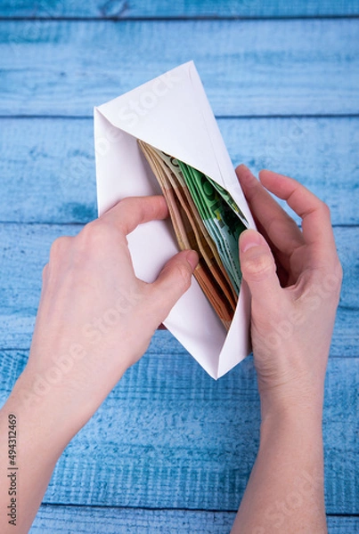 Fototapeta Hands holding an open envelope with money on a blue background