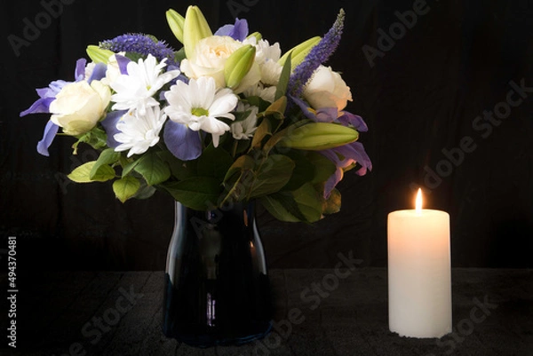 Obraz Funeral Bouquet purple White flowers and burning white candle, Sympathy and Condolence Concept on black background with copy space.