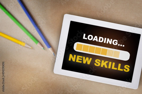 Fototapeta New skills loading on computer digital tablet with coloured pencil on desk. Reskilling and upskilling concept and technology transformation learning