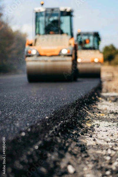 Fototapeta Blurred background of vibratory asphalt rollers compactor compacting new asphalt pavement. Road service building new highway
